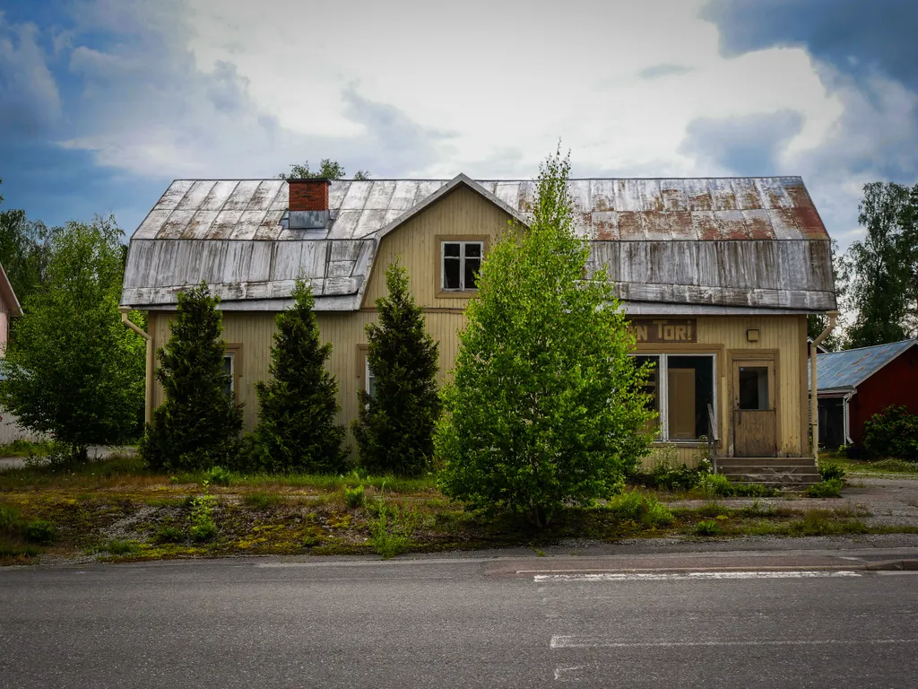 Vor einem alten, in die Jahre gekommenen, gelben Holzhaus stehen ein paar Bäume