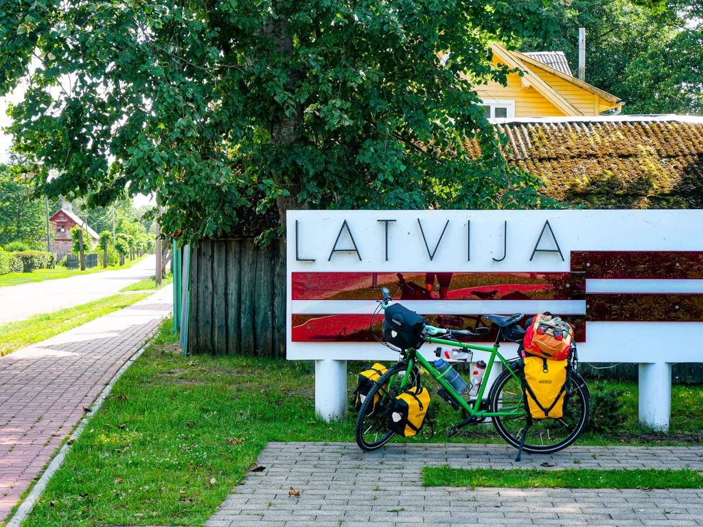 Mein Fahrrad steht an der lettischen Grenze vor einem Schild auf dem in Großbuchstaben "LATVIJA" steht.