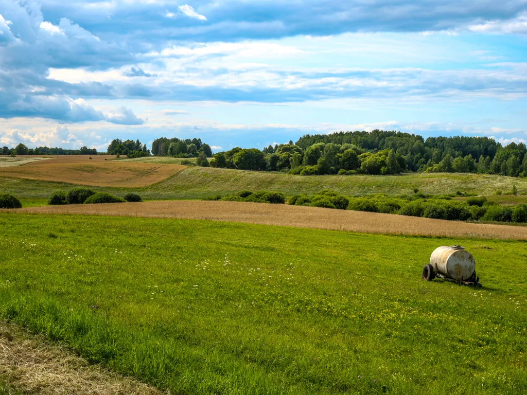 Grüne und Braune Felder mit sanften Hügeln. Im Hintergrund ein Wald. Auf der einem Feld steht ein Güllefass.