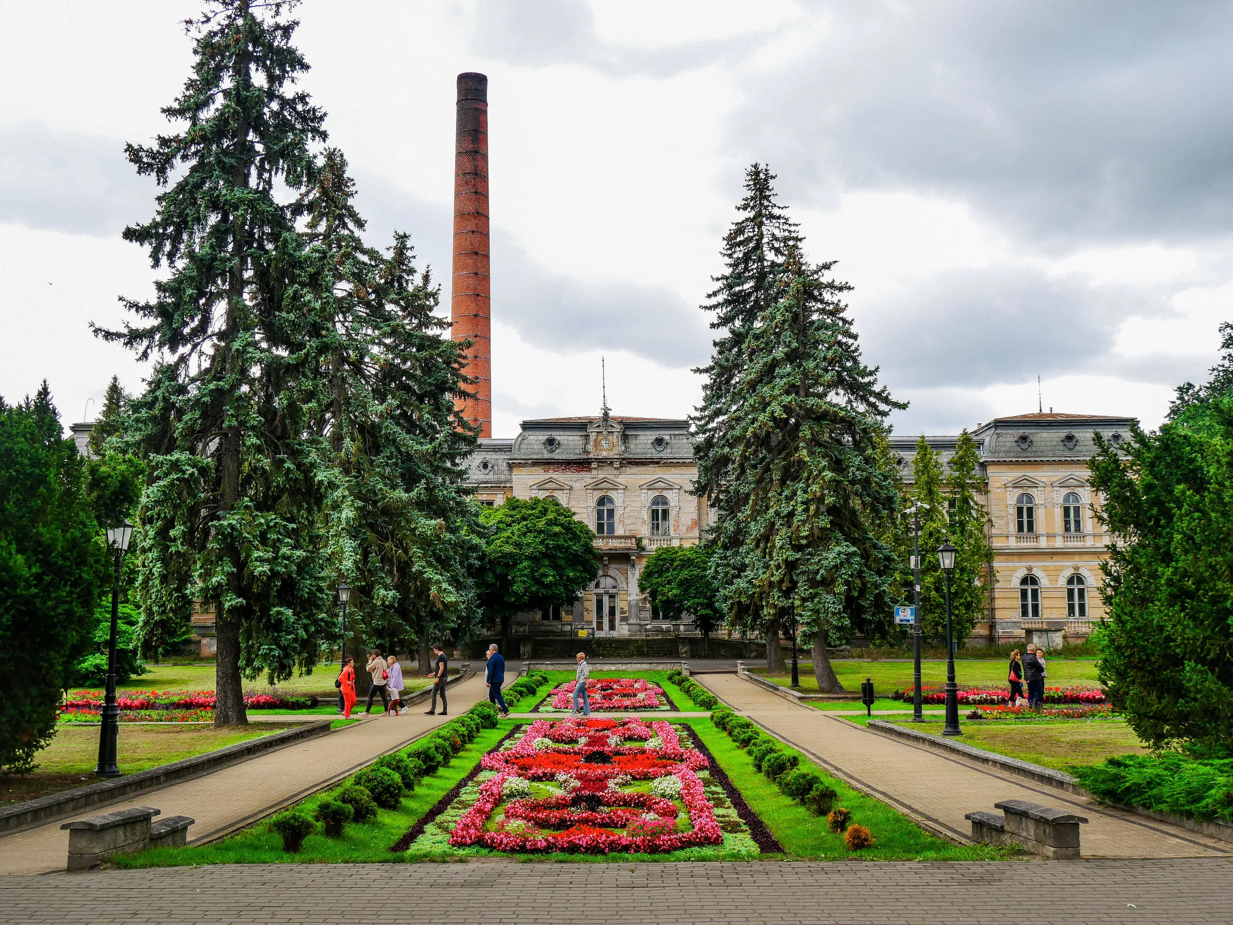 Altes Gebäude mit großem, industriellem Schornstein. Davor ein schön gestaltetes Blumenbeet.