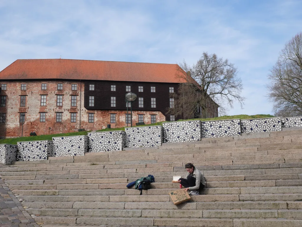 Miri sitzt auf einer Treppe in Kolding und zeigt die viel zu große Riesenpizza