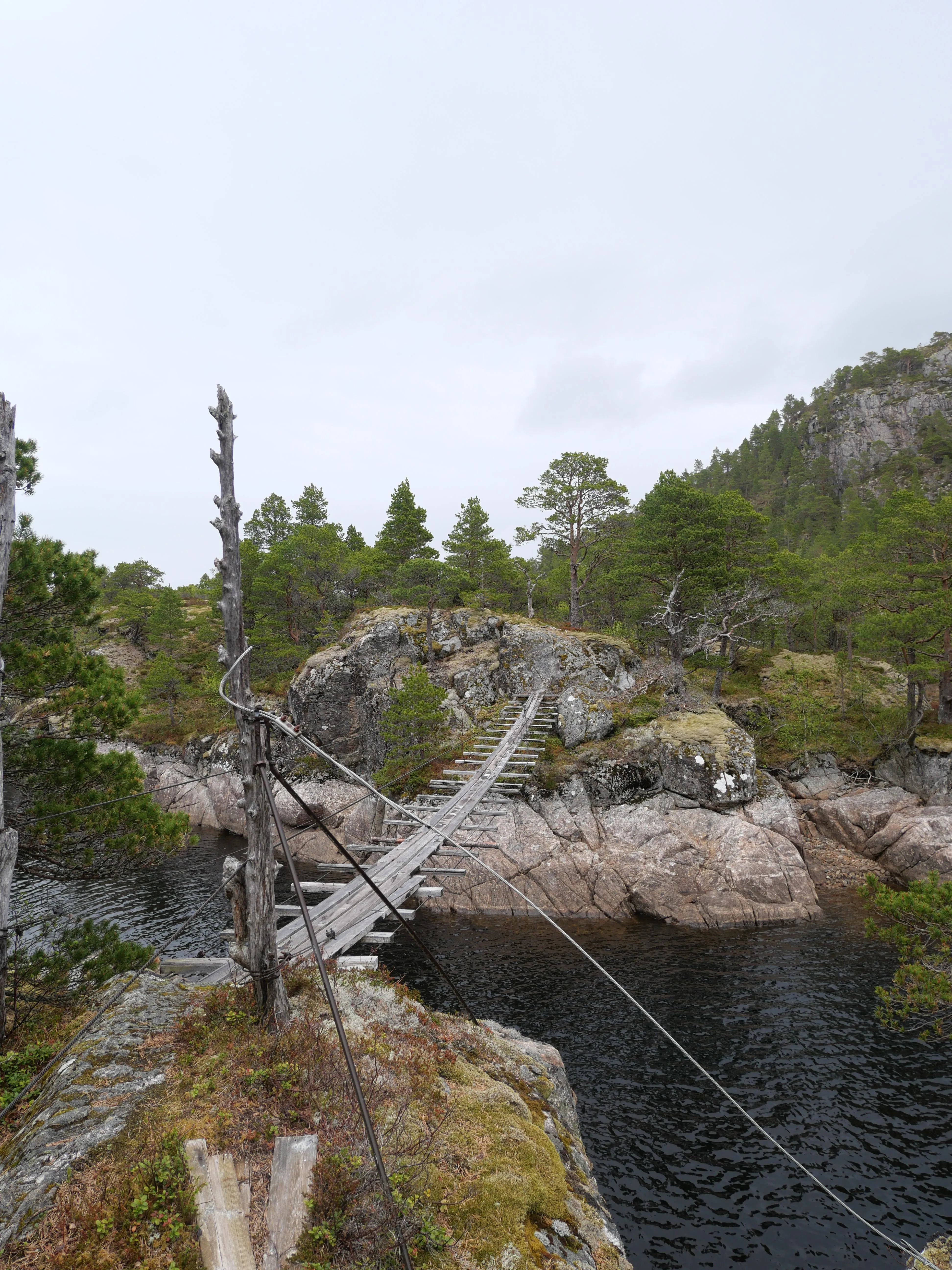 Eine Hängebrücke aus Holz, die schon bessere Tage gesehen hat, verbindet zwei Inseln in einem See.