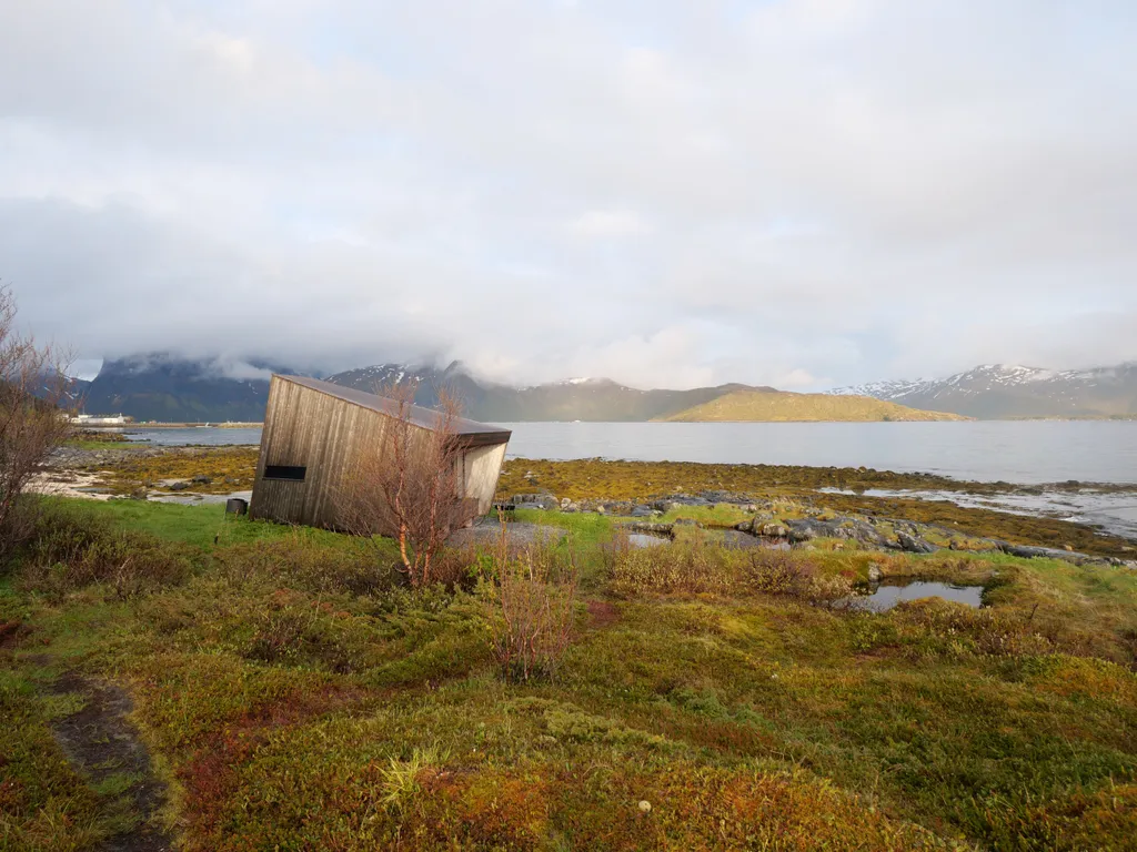 Am Ufer eines Fjords steht ein moderner Unterstand aus Holz.