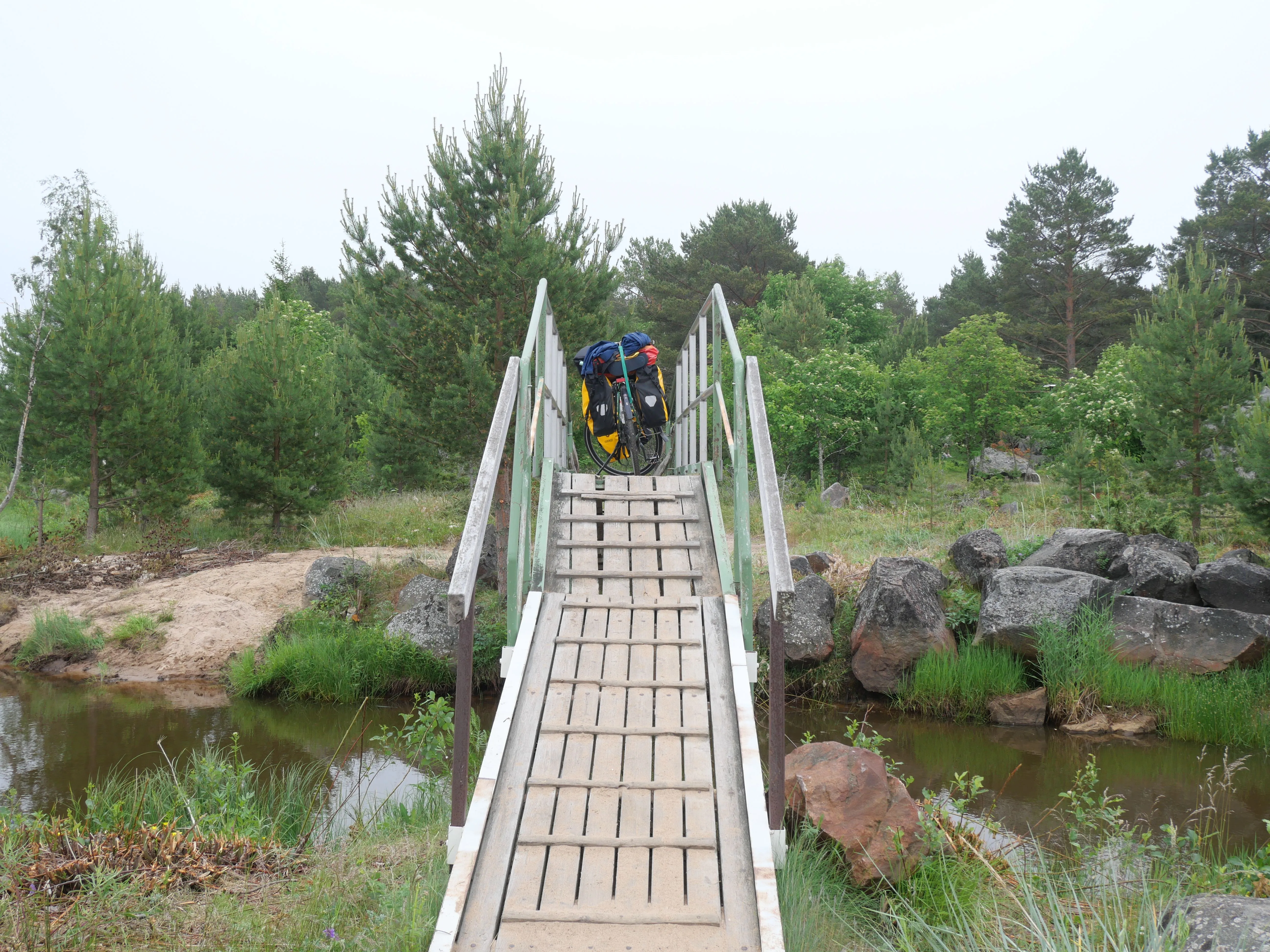 Eine schmale Brücke aus Holz führt über ein Fluss. Mein Fahrrad steht auf der Brücke.